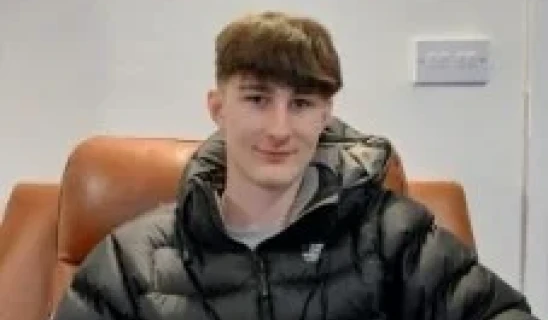 Young man sitting on a brown leather couch wearing a black puffer jacket indoors