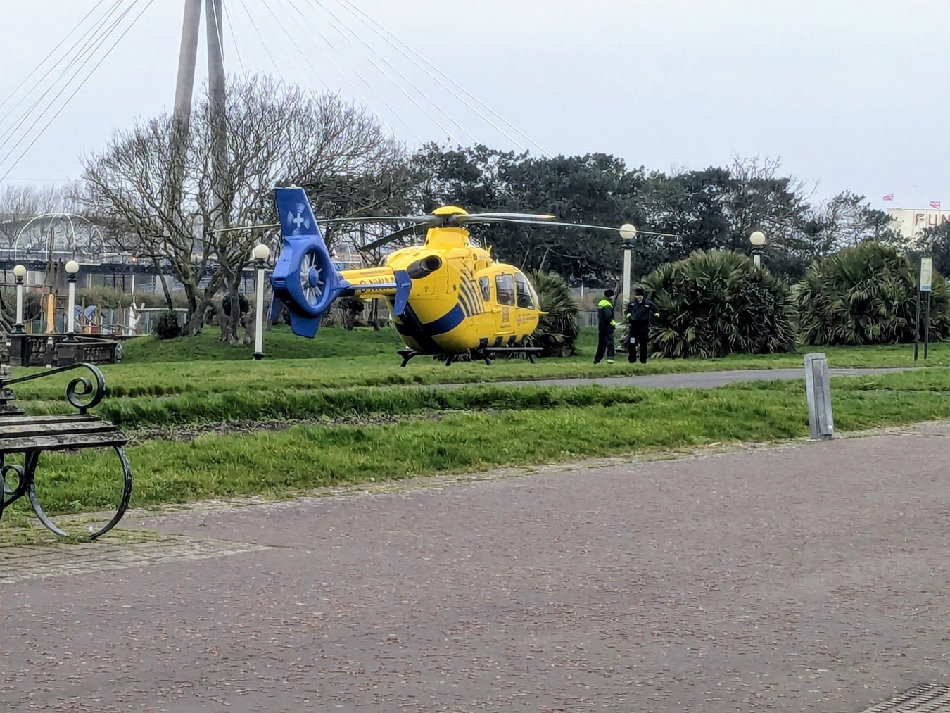 Yellow and blue rescue helicopter landed on grassy area near a promenade.