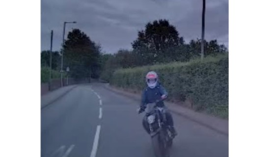 Motorcyclist riding on a suburban road with hedges, wearing a helmet and protective gear.