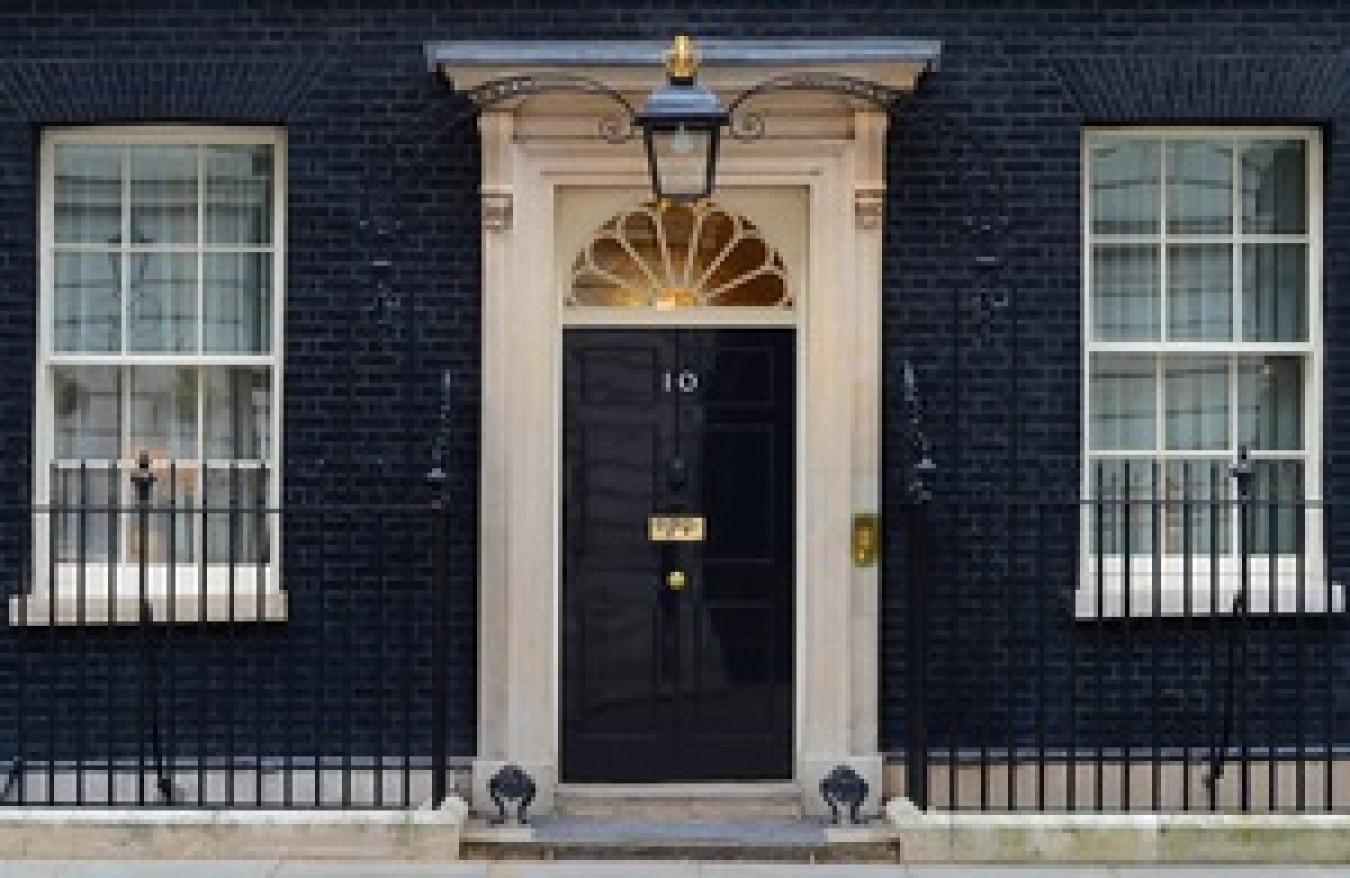 Historic black door with fanlight above, flanked by white-framed windows in a brick building.