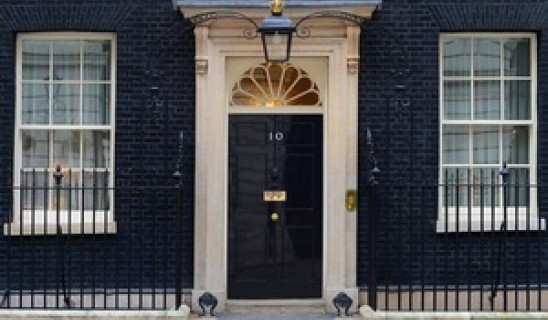 Historic black door with fanlight above, flanked by white-framed windows in a brick building.