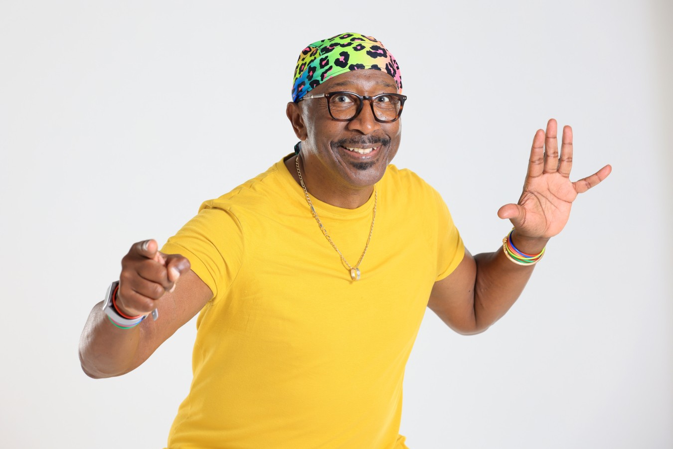 Smiling man wearing a bright yellow shirt and multicoloured headscarf, reaching towards the camera.