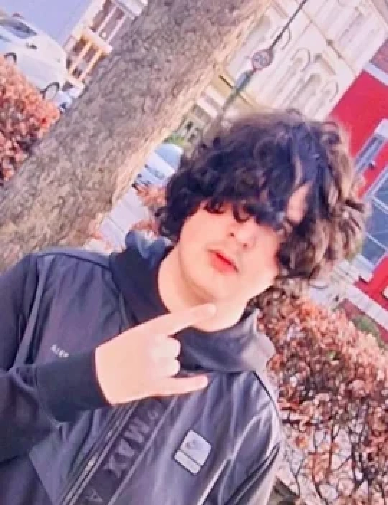 Young person with dark curly hair making a rock-on hand gesture outdoors
