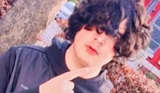 Young person with dark curly hair making a rock-on hand gesture outdoors