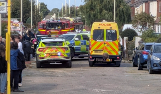 Emergency vehicles including police car, ambulance, and fire engine on a residential street with onlookers
