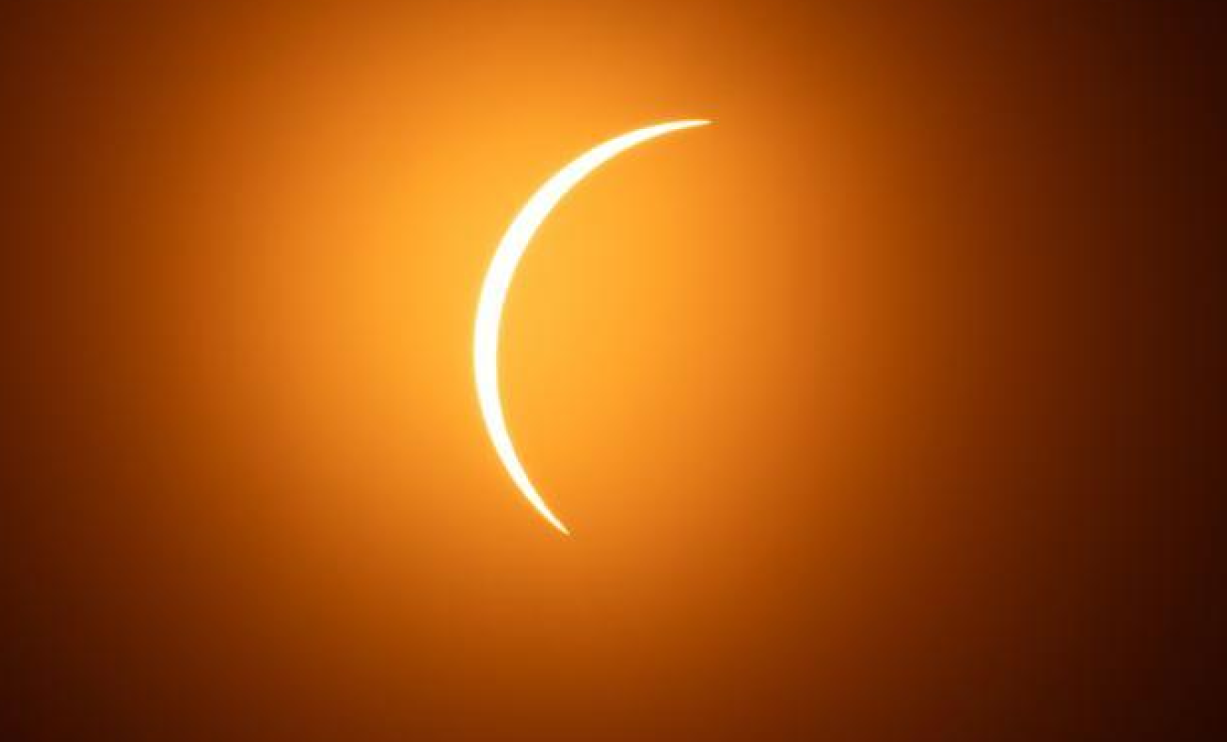 Solar eclipse with a bright crescent against a dark orange sky