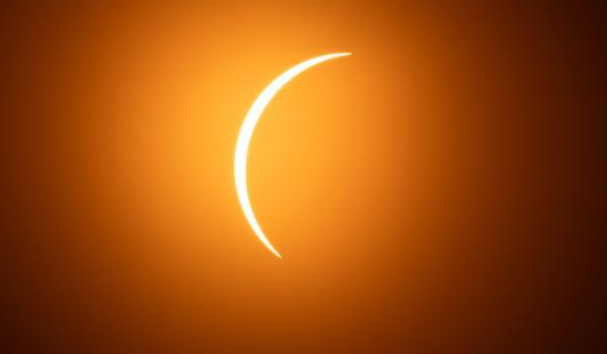 Solar eclipse with a bright crescent against a dark orange sky