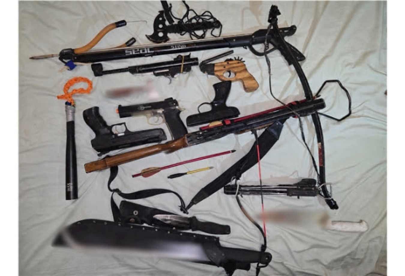Collection of disassembled archery and hunting gear laid out on a light sheet, with bows, grips, strings and accessories.