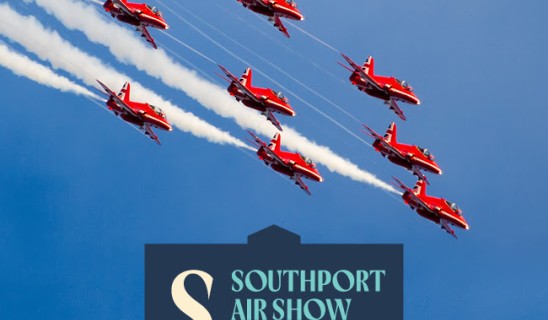 Formation of red aerobatic aircrafts in a blue sky with smoke trails above a Southport Air Show 2026 sign