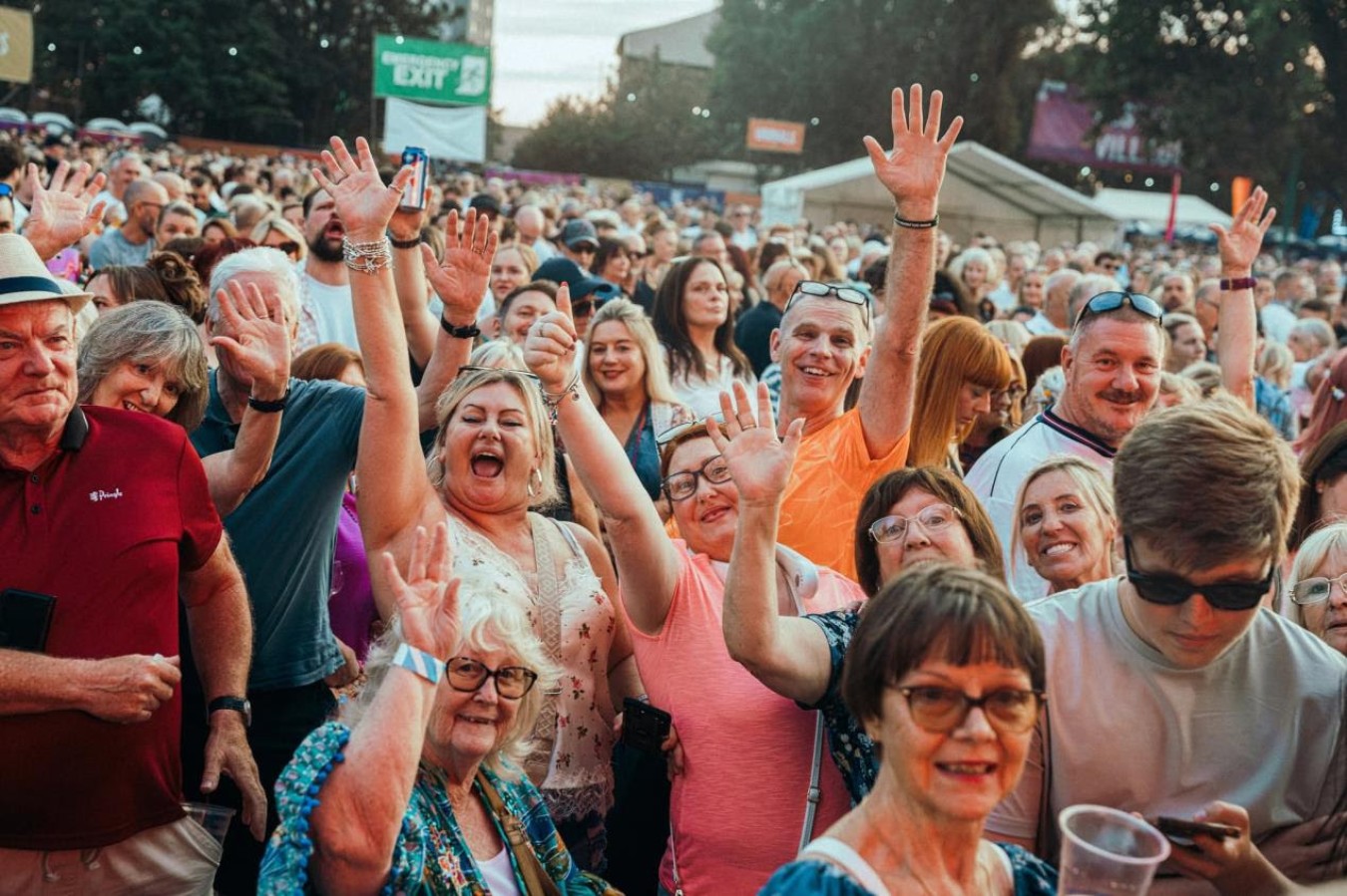 crowd at an outdoor event waving and smiling, many hands raised