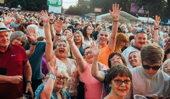 crowd at an outdoor event waving and smiling, many hands raised