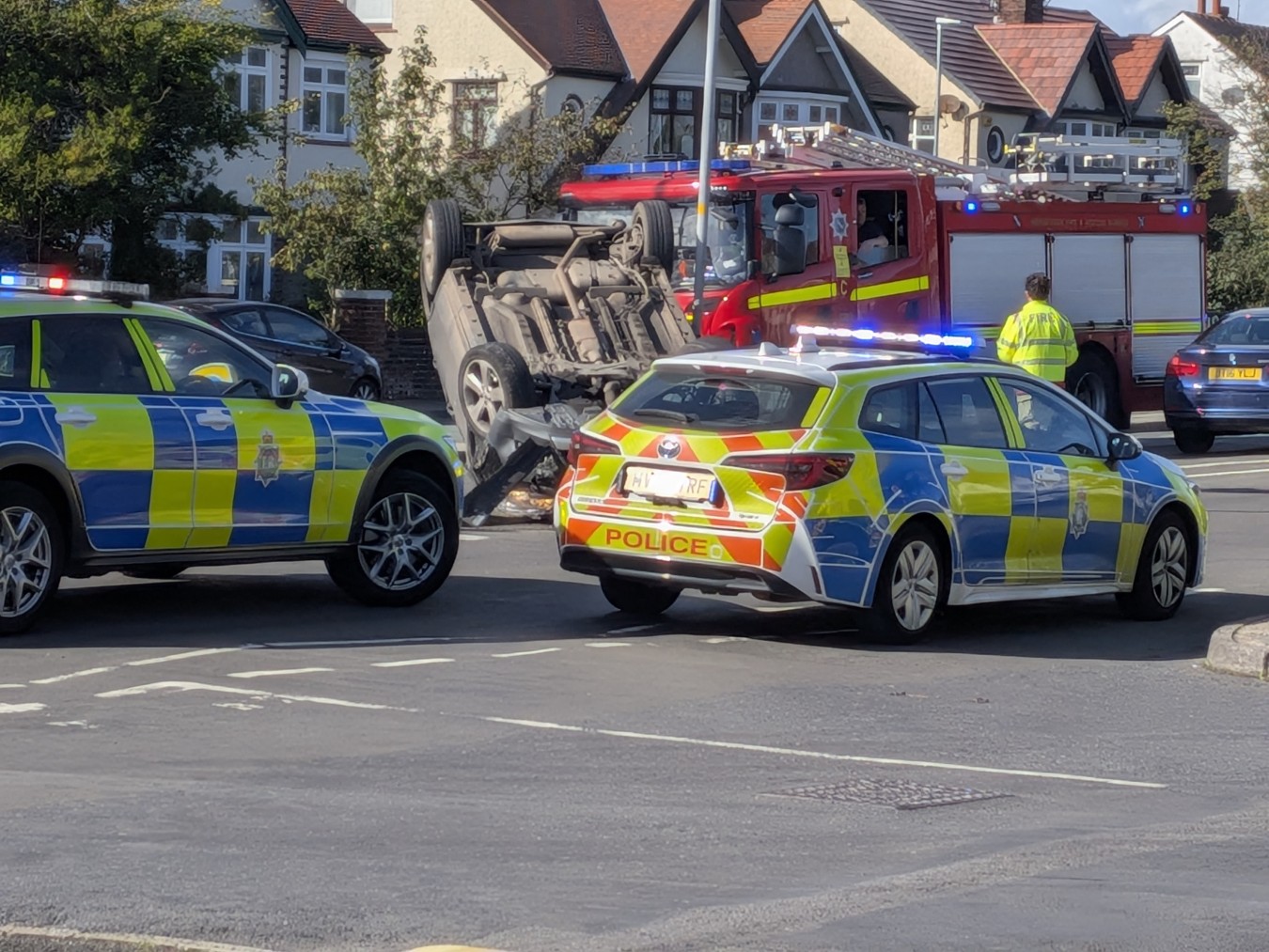 overturned car on its roof amid emergency services at a residential street