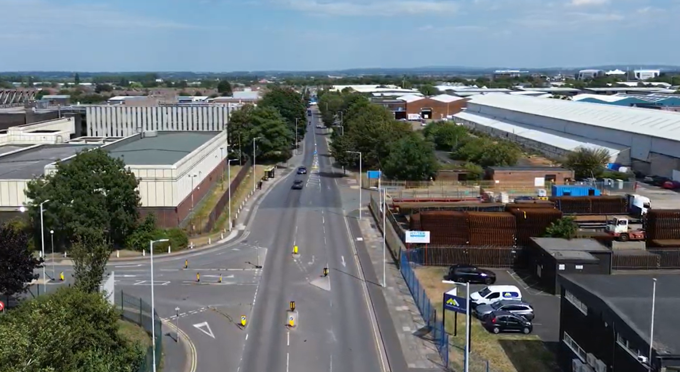 Aerial view of a city street lined with trees, industrial buildings and warehouses on both sides.
