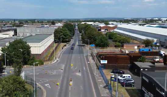 Aerial view of a city street lined with trees, industrial buildings and warehouses on both sides.