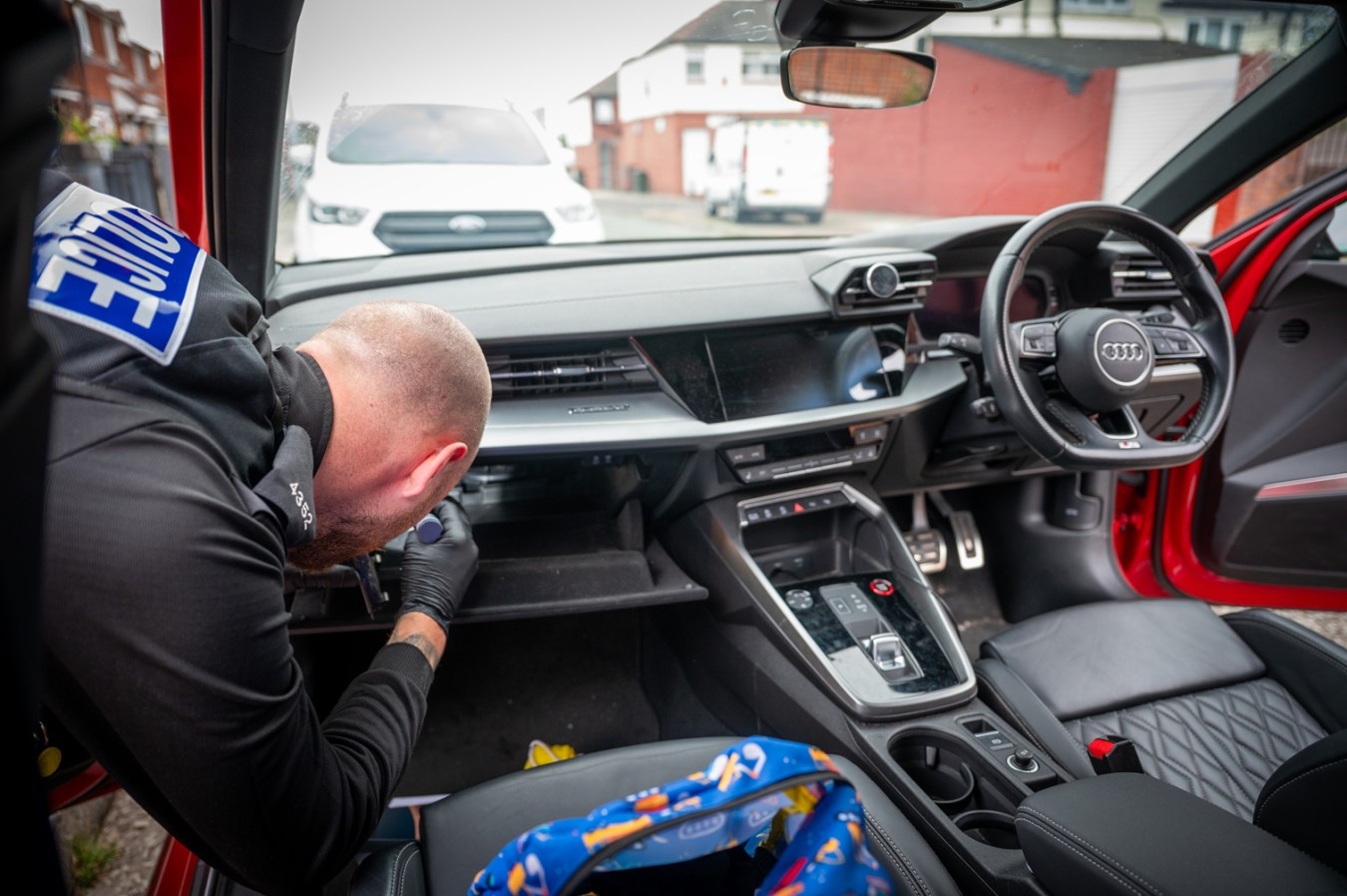 Emergency responder inspecting car dashboard inside a red Audi, driver-side door open.