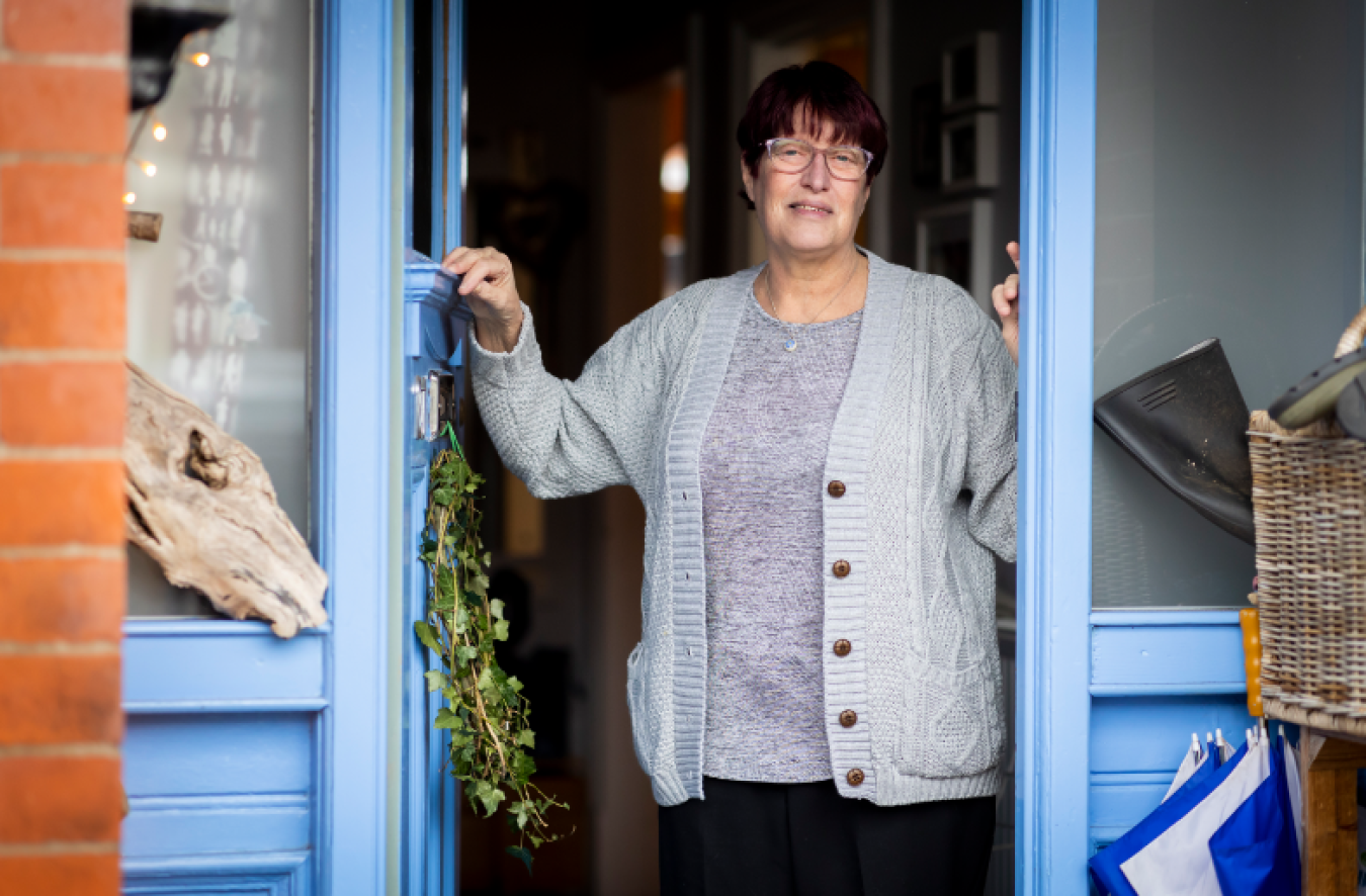 woman standing in doorway of blue-framed shop, holding door frame, smiling at camera