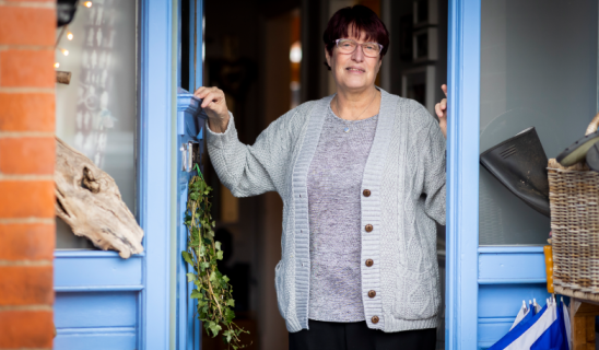 woman standing in doorway of blue-framed shop, holding door frame, smiling at camera