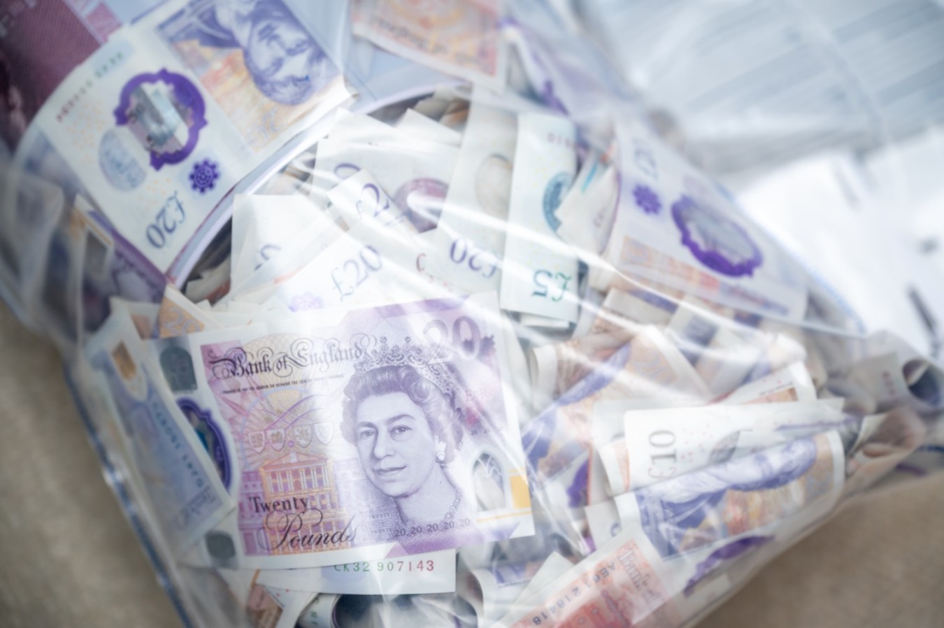 Bag filled with assorted banknotes, primarily British pounds, loosely packed and visible through a transparent cover.