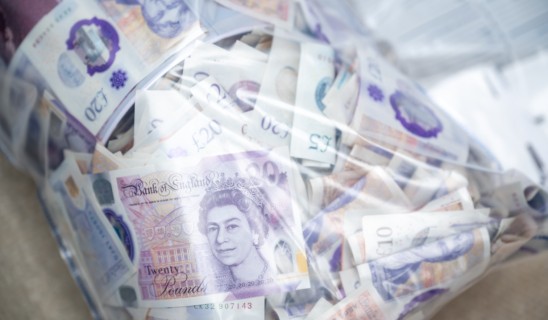 Bag filled with assorted banknotes, primarily British pounds, loosely packed and visible through a transparent cover.