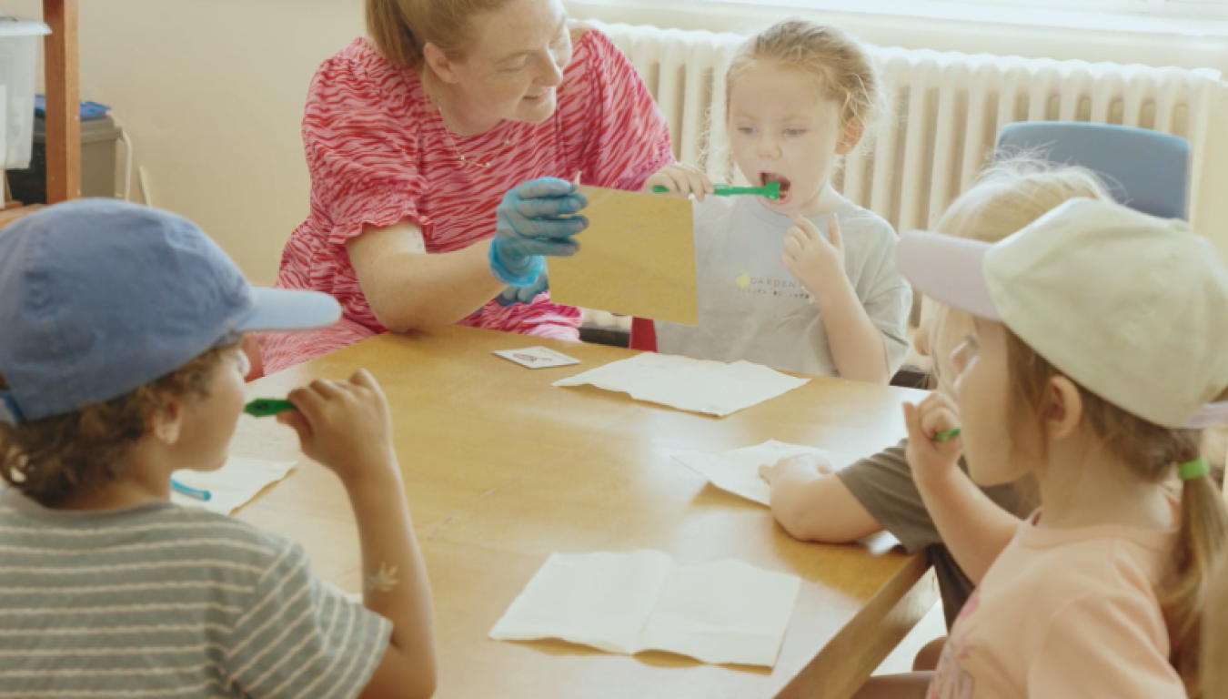Adult assisting children around a table with paper crafts in a bright room.