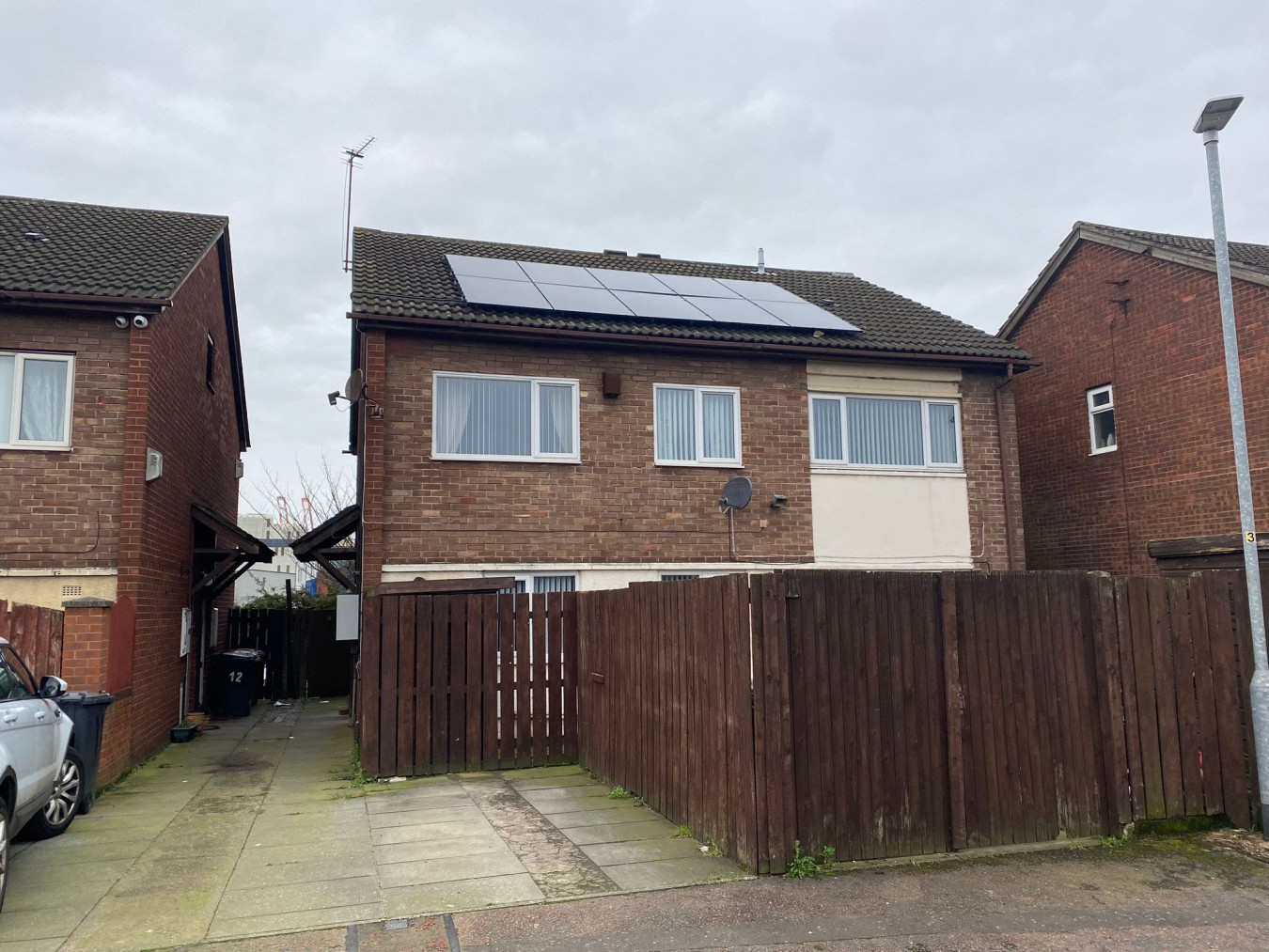 Rear view of brick houses with solar panels on roof and brown wooden fence in foreground.