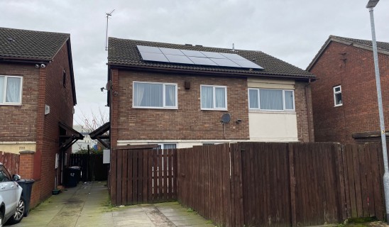 Rear view of brick houses with solar panels on roof and brown wooden fence in foreground.