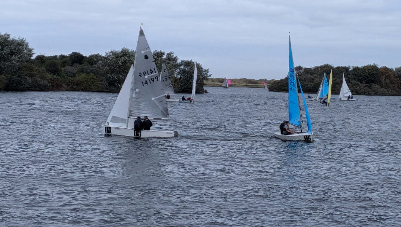 Sailing boats on a calm lake with a group of people on board and small sail colors in the distance.