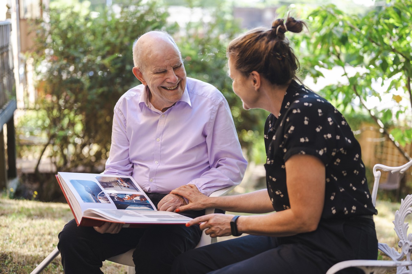 Smiling elderly man and woman looking through a photo album outdoors in garden
