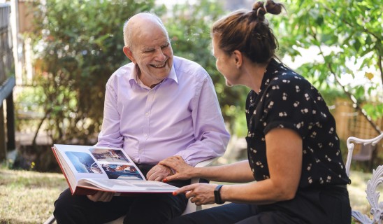 Smiling elderly man and woman looking through a photo album outdoors in garden