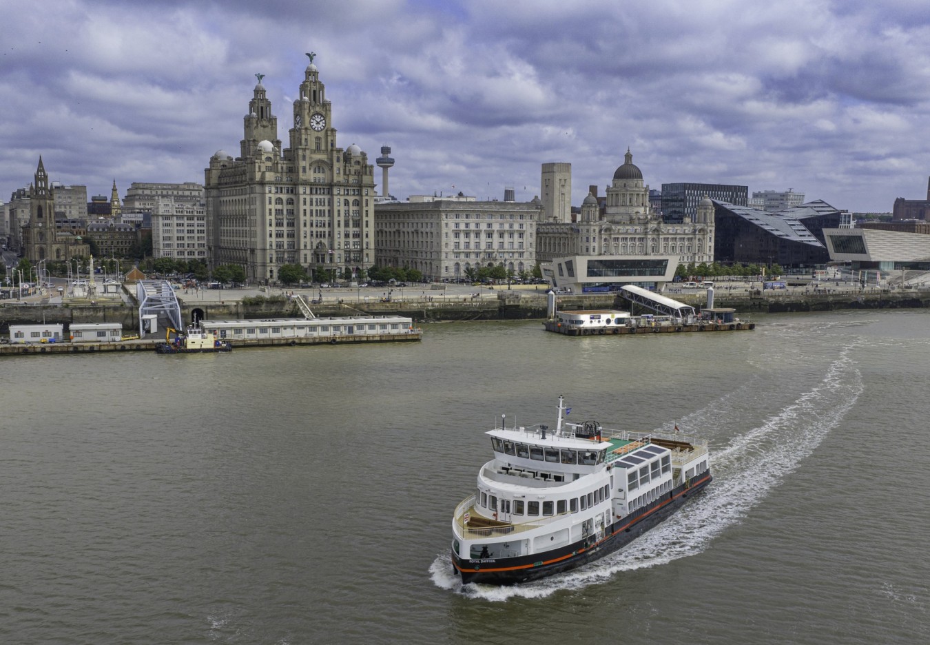 Liverpool waterfront with historic buildings along the river and a large white passenger vessel in the foreground.