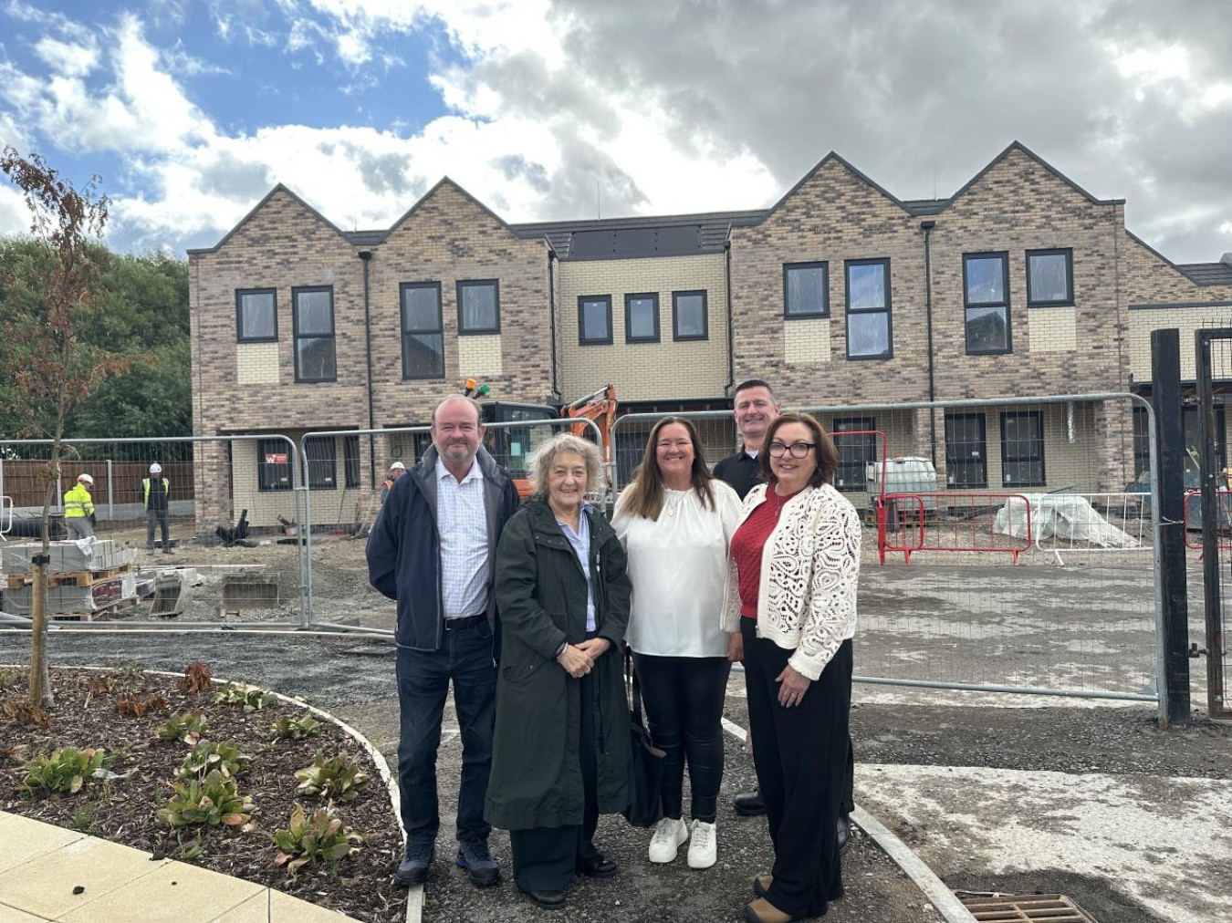 Group of five adults standing in front of a construction site with a brick building under development.