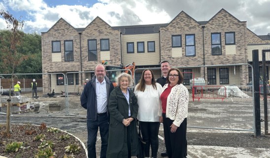 Group of five adults standing in front of a construction site with a brick building under development.