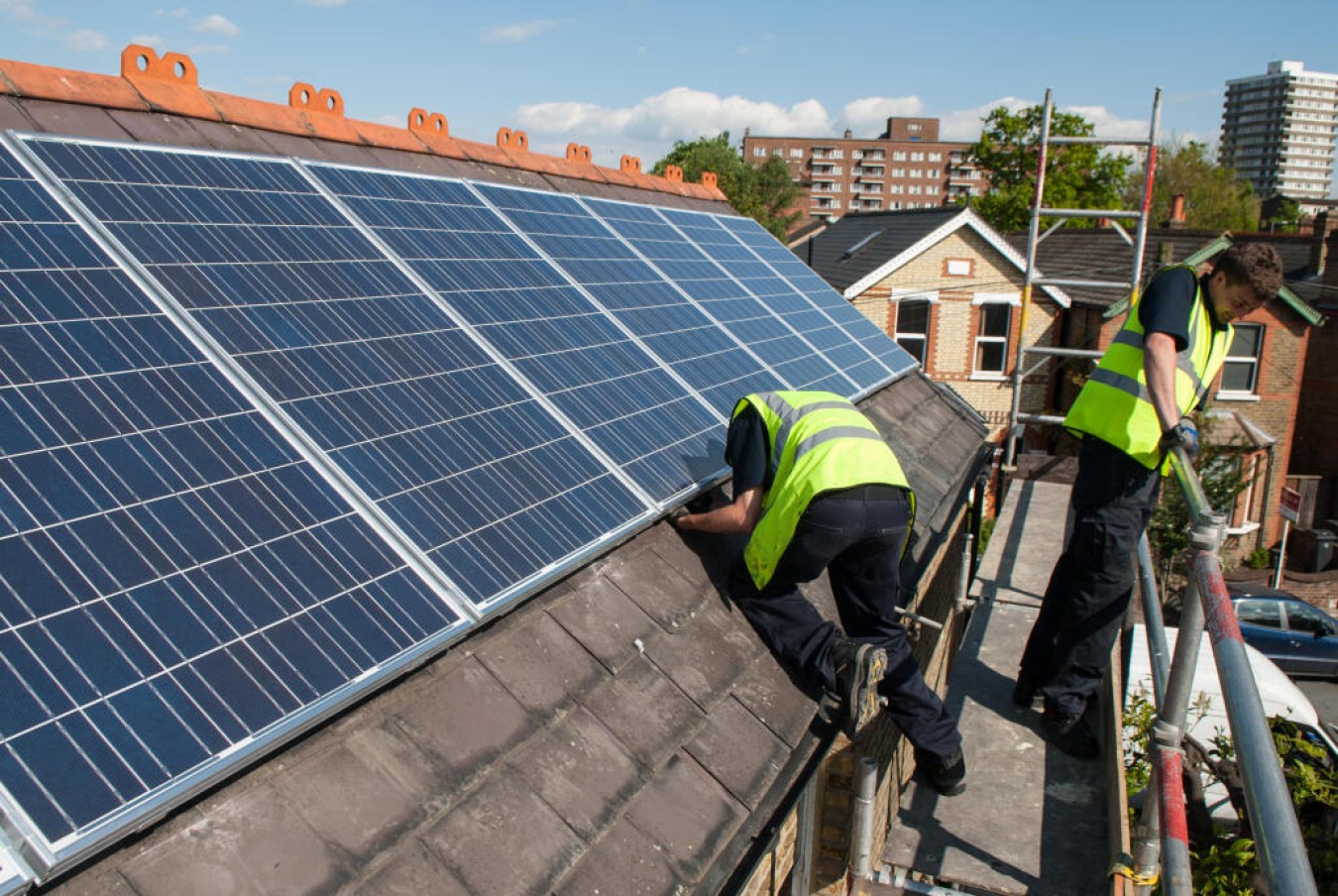 Two workers in high-visibility vests install or inspect solar panels on a sloped roof.