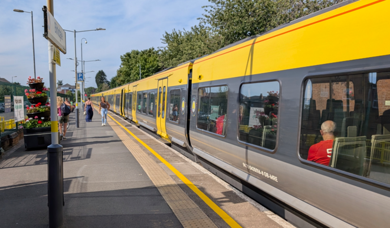 Bright yellow passenger train at platform with people boarding and waiting during sunny day