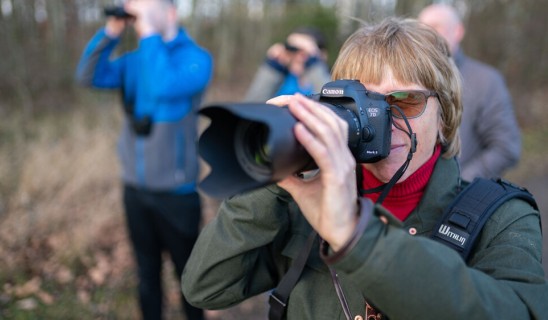 Photographer aiming a Canon camera with lens hood in a woodland setting