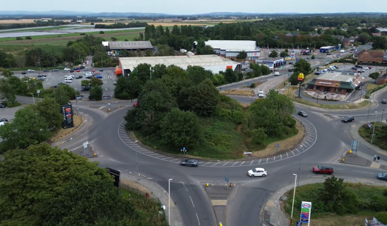 Aerial view of a roundabout with surrounding shops, cars, and green trees.