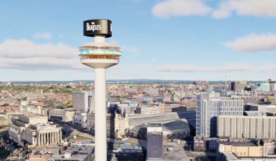 Aerial view of a city with a tall observation tower in the foreground featuring a circular top adorned with a Beatles sign.