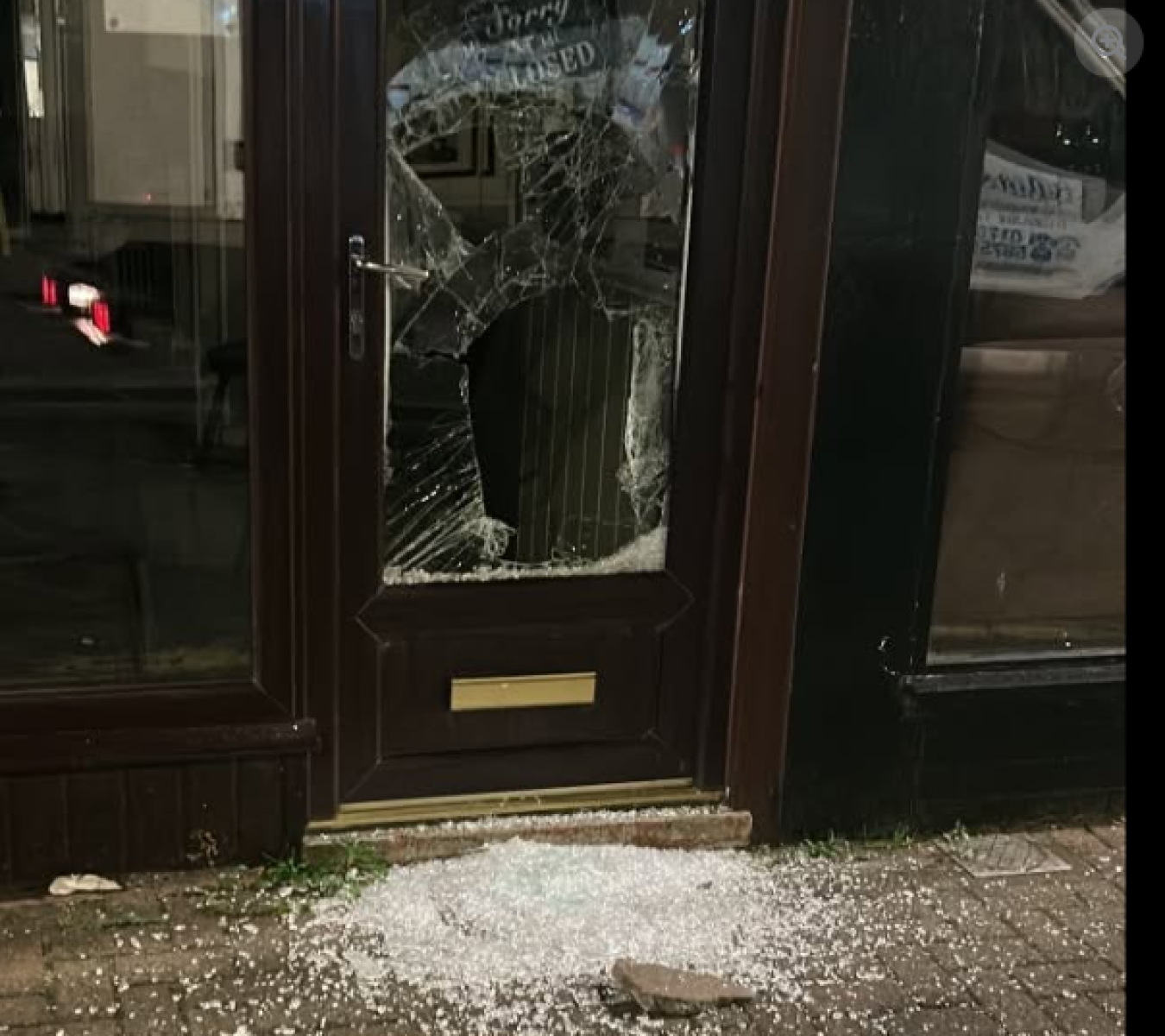 Shattered glass door with broken window, debris on doorstep and pavement outside.