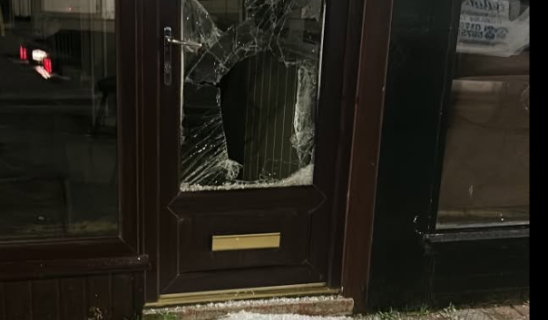 Shattered glass door with broken window, debris on doorstep and pavement outside.