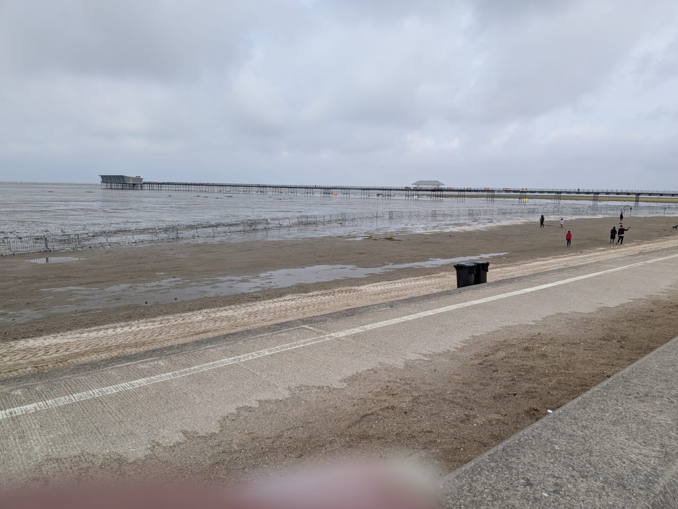 Long pier extends over tidal flats with a pavilion at the far end and a cloudy sky above