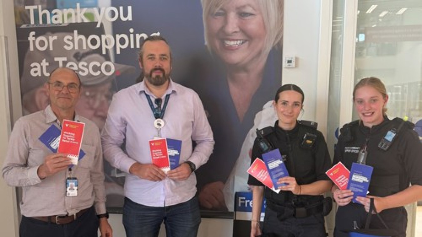 Group of four people in a Tesco store lobby holding red and blue leaflets.
