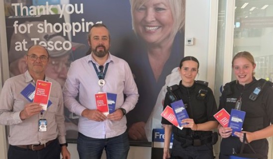 Group of four people in a Tesco store lobby holding red and blue leaflets.