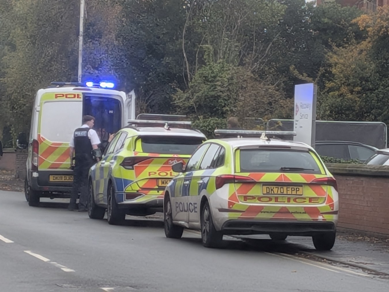 Police cars and an ambulance parked on a street with blue lights flashing.