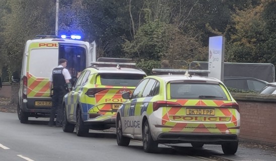 Police cars and an ambulance parked on a street with blue lights flashing.