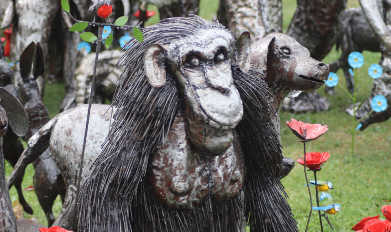 Iron sculpture of a monkey with long hair and a smiling face in a garden exhibition.