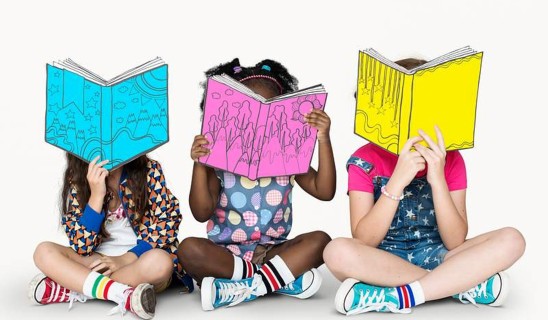 Three children sitting cross-legged, reading colourful illustrated books over their faces.