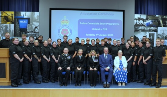 Police cadets in black uniforms posing with dignitaries on stage during ceremony.
