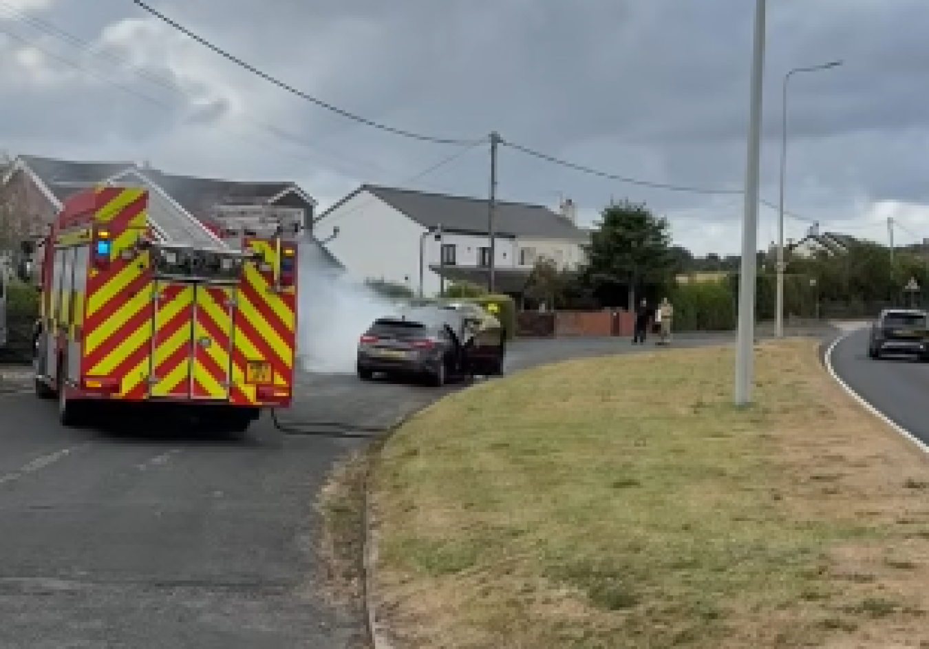 Emergency services vehicle on a suburban street with a person near a car and a curved road