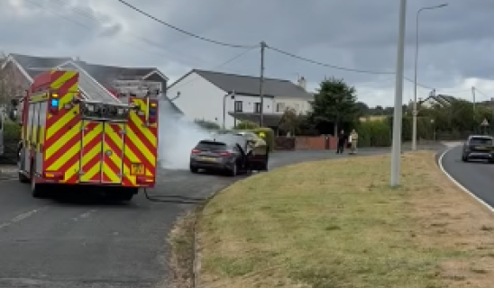 Emergency services vehicle on a suburban street with a person near a car and a curved road