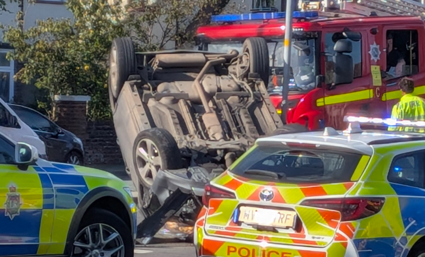 Car flipped on its roof with emergency vehicles, police and fire appliances at accident scene.
